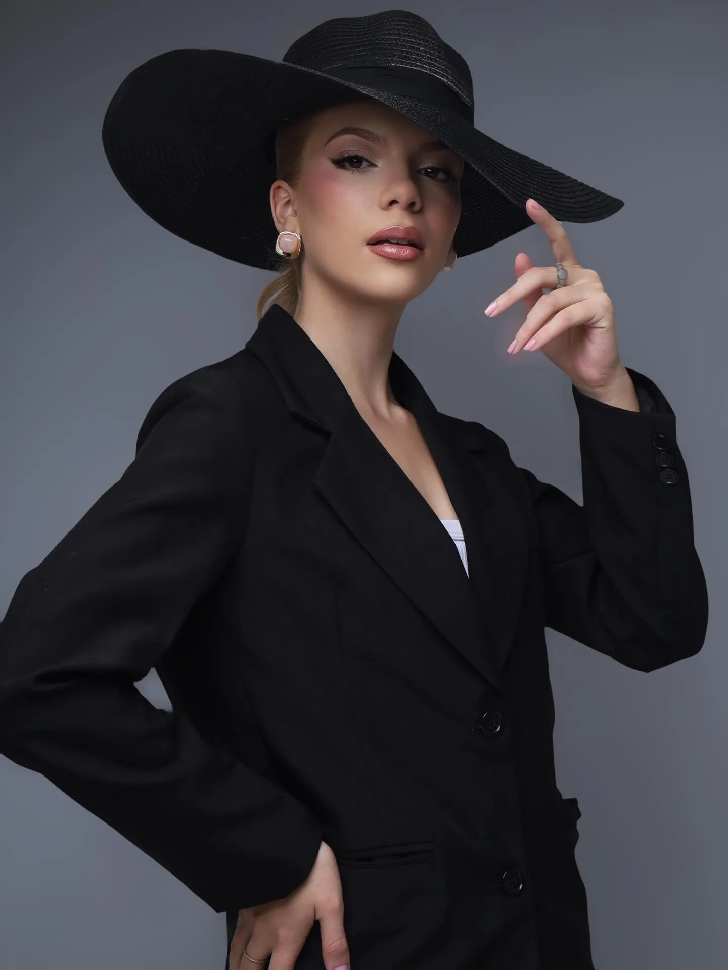 Mulher com chapéu preto e blazer em um retrato de fundo cinza