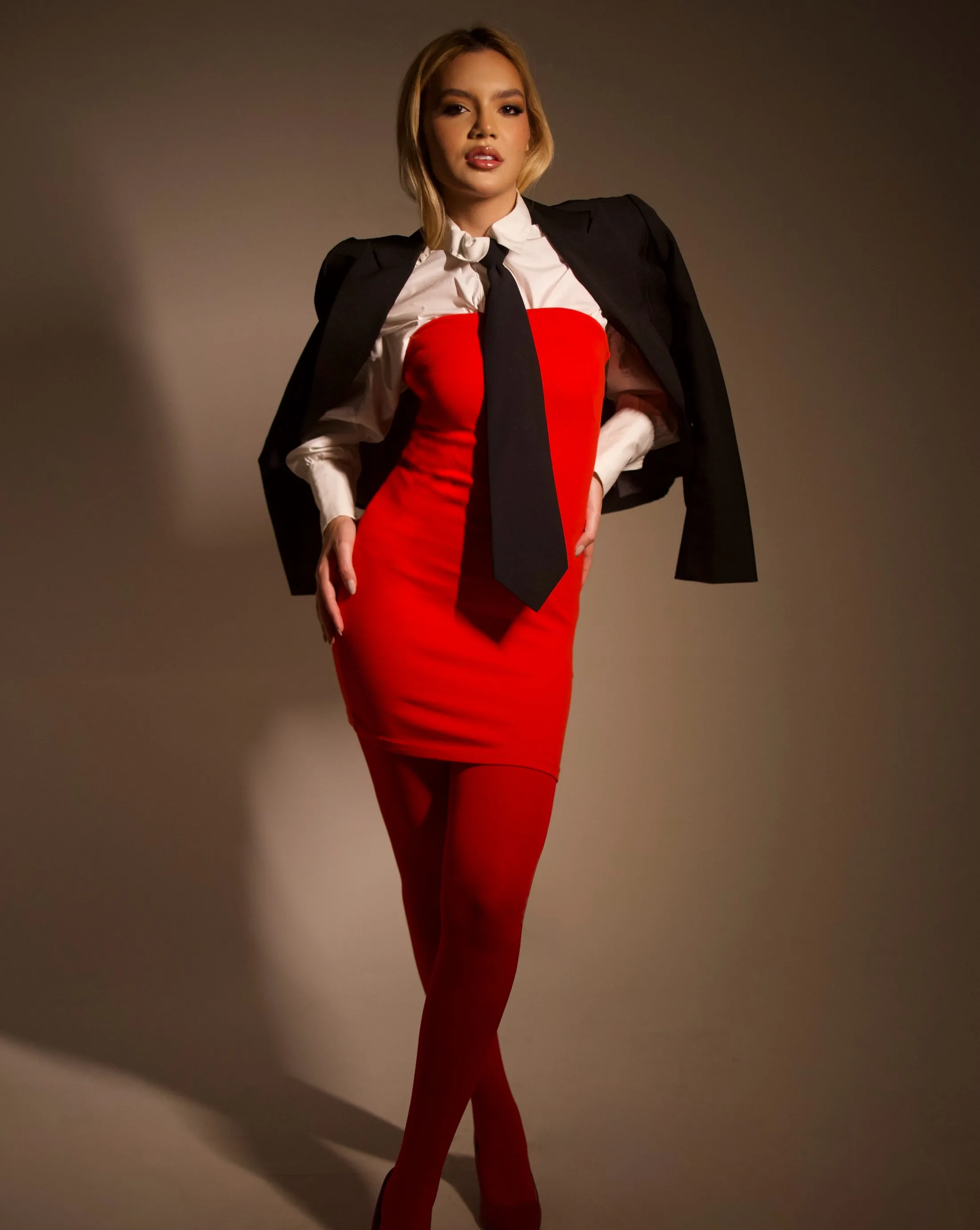 Mulher de macacão vermelho com camisa branca e blazer preto sob luz lateral