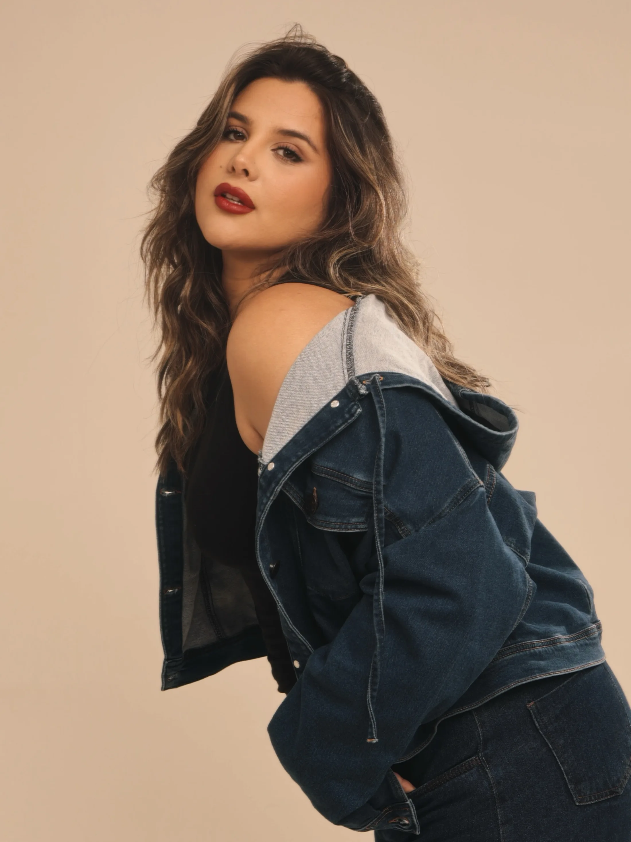 Mulher de jaqueta jeans olhando sobre o ombro em fundo neutro
